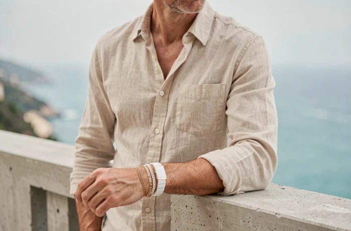 Homme portant des bracelets empilés en or blanc sur une terrasse avec vue sur la mer Méditerranée